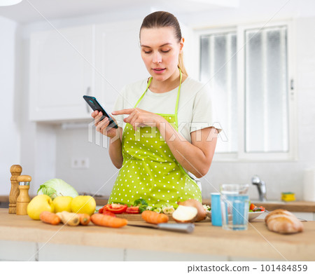 Housewife looking for recipe on internet using smart phone in the kitchen 101484859