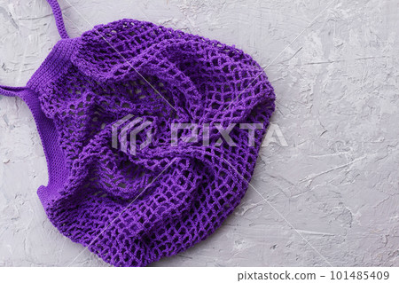 knitted purple mesh string bag, gray concrete background with beads of plaster knitted purple mesh string bag, gray concrete background with beads of plaster 101485409