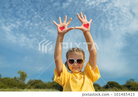 little girl 5 years old in yellow blouse raised hands up with red hearts on background of sky 101485413