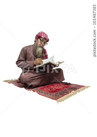 Muslim man with a beard wearing keffiyeh with agal sitting and reading the Quran on the prayer rug 101487383