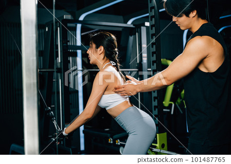 Smiling coach instructing a woman on how to use a pull-down weight machine, focusing on building muscular strength and endurance. GYM healthy lifestyle concept 101487765