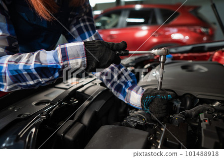 Female auto mechanic unscrewing a nut to replace a car spark plug. 101488918