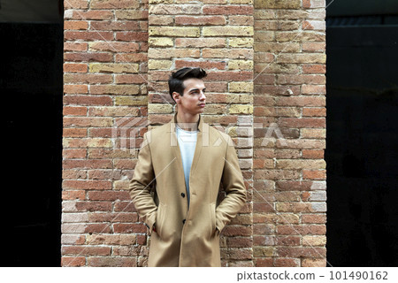 Young man wearing winter clothes in the street. Young guy with modern hairstyle with brown coat. 101490162