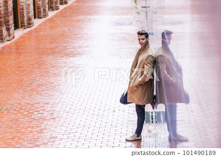 Portrait of stylish handsome young man with coat standing outdoors and leaning on wall. 101490189