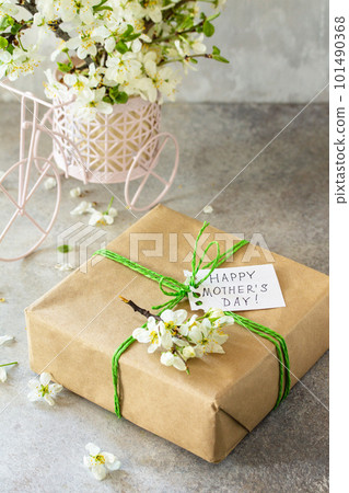Mother's day or womens day background. Blooming cherry branch and a present with a congratulatory inscription that Happy Mother's Day on a gray stone table. Copy space. Mother's day or womens day background. Blooming cherry branch and a present with a congratulatory inscription that Happy Mother's Day on a gray stone table. Copy space. 101490368