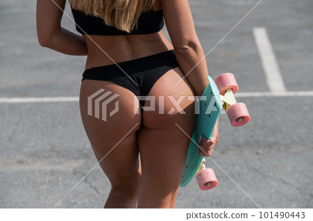 Close-up of the buttocks of a caucasian woman in a swimsuit holding a penny board. Athletic girl with a seductive figure.  101490443