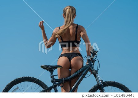 Caucasian woman with a stunning athletic figure in short shorts rides a bike against the blue sky 101490445