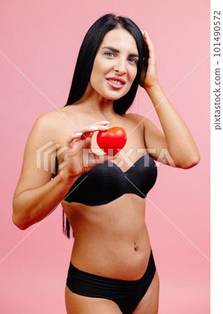 Happy young sexy woman wearing black swimsuit holding red heart in hands isolated on pink color background studio. Summer rest concept Happy young sexy woman wearing black swimsuit holding red heart in hands isolated on pink color background studio. Summer rest concept 101490572