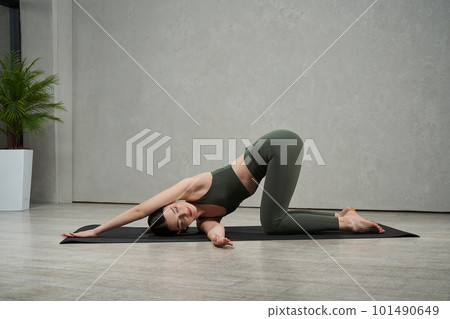 Side view of slim, flexible female athlete working out, exercising, training indoors. Young, brunette girl stretching barefoot. Concept of athletics, sport and wellbeing. 101490649