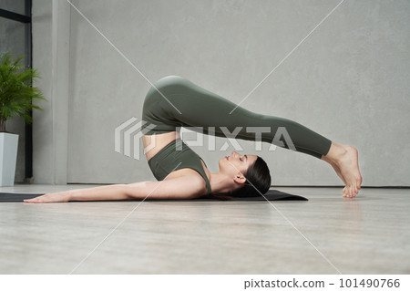Side view of flexible girl wearing sportswear training, exercising, doing yoga in studio. Young, brunette woman wearing sportswear, stretching. Concept of yoga and harmony. Side view of flexible girl wearing sportswear training, exercising, doing yoga in studio. Young, brunette woman wearing sportswear, stretching. Concept of yoga and harmony. 101490766
