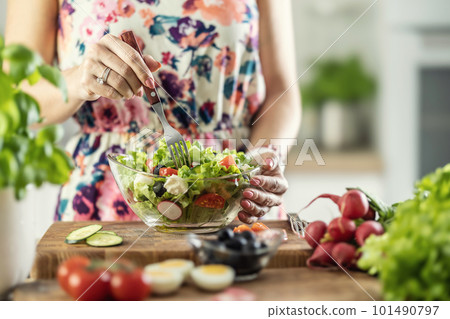 A young woman tastes a healthy salad with a fork in her kitchen 101490797