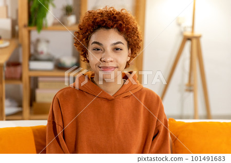 Beautiful african american girl with afro hairstyle smiling sitting on sofa at home indoor. Young african woman with curly hair smiling. Freedom happiness carefree happy people concept 101491683