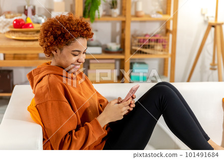 African girl holding smartphone touch screen typing scroll page at home. Woman with cell phone surfing internet using social media apps playing game. Shopping online Internet news cellphone addiction 101491684