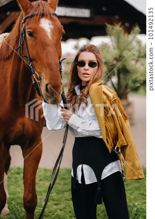Stylish girl with glasses stands next to a horse on the street 101492135