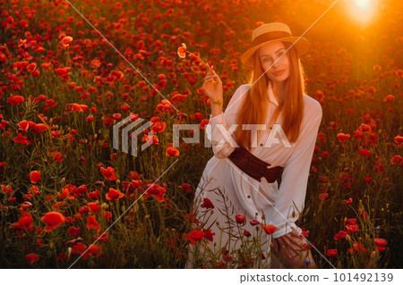 a girl in a white dress and hat stands in a field with poppies at sunset and holds a poppy flower in her hand a girl in a white dress and hat stands in a field with poppies at sunset and holds a poppy flower in her hand 101492139
