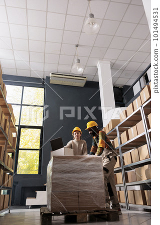 Multi ethnic group of people wearing industrial overall and helmet working in storage room, preparing customers orders for shipping. Storage room workers checking delivery detalis on laptop computer. Multi ethnic group of people wearing industrial overall and helmet working in storage room, preparing customers orders for shipping. Storage room workers checking delivery detalis on laptop computer. 101494531