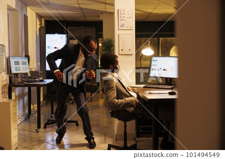 Funny manager scares his sleepy colleague in startup office, worker falling asleep on desk in startup office. African american employees working late at night at marketing strategy Funny manager scares his sleepy colleague in startup office, worker falling asleep on desk in startup office. African american employees working late at night at marketing strategy 101494549