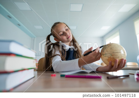 Caucasian schoolgirl sits at her desk at school and studies the globe. Caucasian schoolgirl sits at her desk at school and studies the globe. 101497118