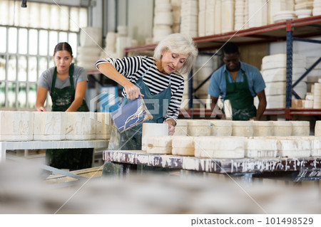 Mature worker pours slip mass from jug into plaster mold in pottery factory Mature worker pours slip mass from jug into plaster mold in pottery factory 101498529
