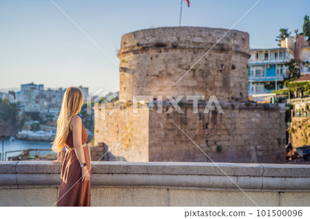 Woman tourist on background of Hidirlik Tower in Antalya against the backdrop of the Mediterranean bay of the ancient Kaleici district, Turkey. Turkiye 101500096