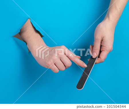 Woman filing her nails through a hole on a blue background. Woman filing her nails through a hole on a blue background. 101504344
