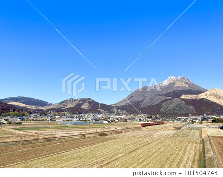 A red train running with a sunny blue sky and Mt. Yufu in the background A red train running with a sunny blue sky and Mt. Yufu in the background 101504743