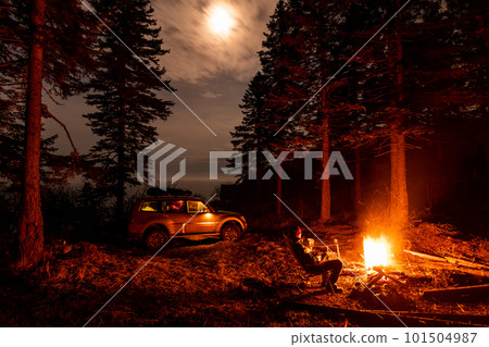 A man sitting at campfire in a tourist camp in a fir forest near the sea. A man sitting at campfire in a tourist camp in a fir forest near the sea. 101504987
