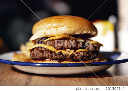Rustic cheeseburger with cheese and meat on a wooden table in a restaurant. Fast food, meat, american cuisine concept. Rustic cheeseburger with cheese and meat on a wooden table in a restaurant. Fast food, meat, american cuisine concept. 101506141