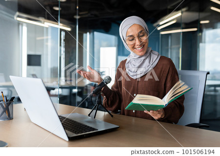 Young beautiful muslim woman in hijab working in modern office using professional microphone to record audio podcast reading religious book online radio. Young beautiful muslim woman in hijab working in modern office using professional microphone to record audio podcast reading religious book online radio. 101506194