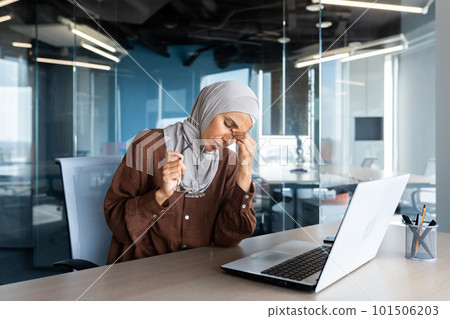 Tired and overworked business woman in hijab at workplace, muslim woman massaging eyes with glasses off, female worker working late on project. 101506203
