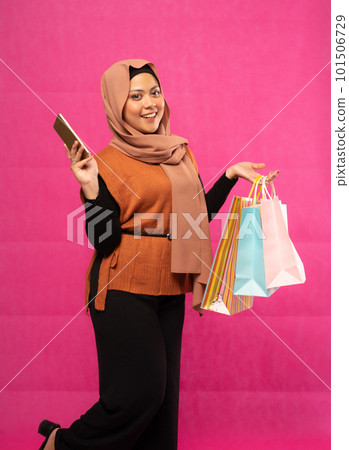 woman in hijab holding mobile phone and carrying shopping bag 101506729