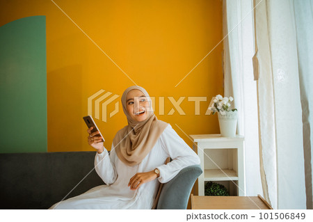 Asian veiled woman casually sitting on sofa using cell phone Asian veiled woman casually sitting on sofa using cell phone 101506849