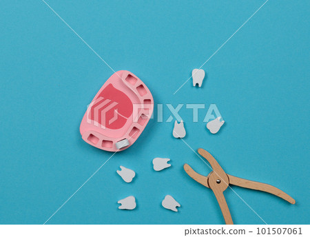 Toy wooden dentist set. Toy jaw with teeth and dentist forceps. Top view on a blue background. 101507061