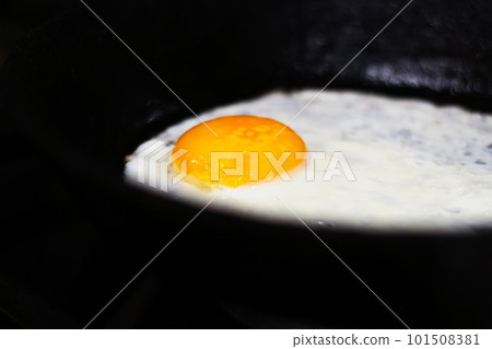 Fried egg on frying pan. Black night. One fried egg in cast iron frying pan sprinkled with ground black pepper. Out of focus Fried egg on frying pan. Black night. One fried egg in cast iron frying pan sprinkled with ground black pepper. Out of focus 101508381