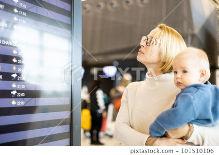 Mother traveling with child, holding his infant baby boy at airport terminal, checking flight schedule, waiting to board a plane. Travel with kids concept 101510106
