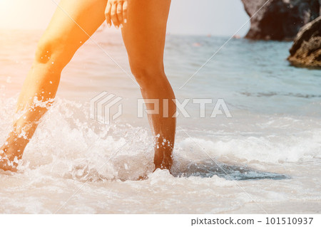Sea beach travel - woman walking on sand beach leaving footprints in the white sand. Female legs walking along the seaside barefoot, close-up of the tanned legs of a girl coming out of the water. 101510937