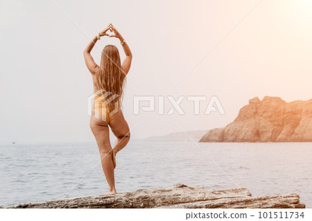 Woman sea yoga. Back view of free calm bliss satisfied woman with long hair standing on top rock with yoga position against of sky by the sea. Healthy lifestyle outdoors in nature, fitness concept. 101511734