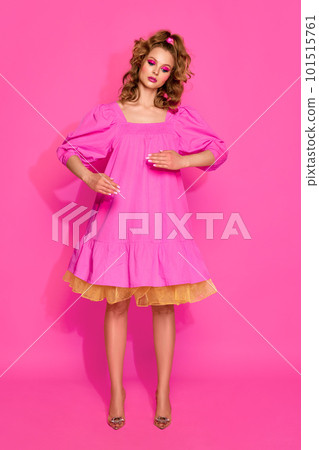 One beautiful blond woman, girl with bright makeup wearing doll dress posing with emotionless face over pink studio background. Living doll One beautiful blond woman, girl with bright makeup wearing doll dress posing with emotionless face over pink studio background. Living doll 101515761