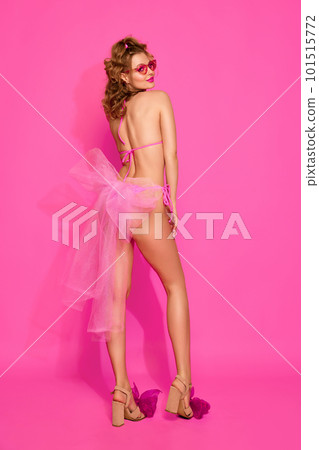 Portrait of blond girl wearing stylish swimsuit and sunglasses posing with joyful face over pink studio background. Woman like a gift. Back view Portrait of blond girl wearing stylish swimsuit and sunglasses posing with joyful face over pink studio background. Woman like a gift. Back view 101515772
