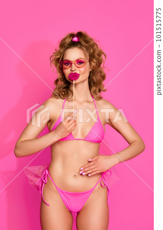 Portrait of young adorable girl wearing swimsuit and posing with candy instead of lips over pink studio background. Funny face 101515775
