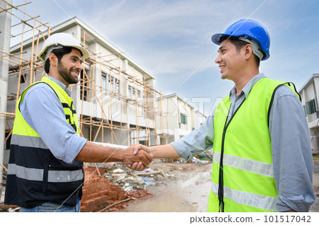 Construction engineer and architect with blueprint shaking hands while standing on construction site. Home building concept. 101517042