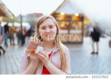 smiling girl in jacket at fair in city eating trdelnik 101517922