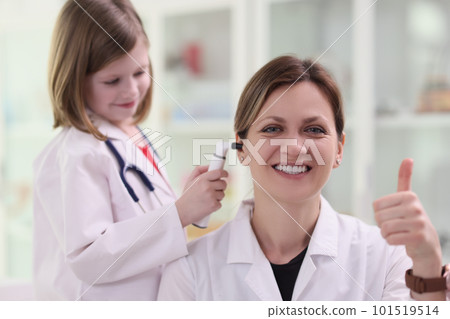 Little girl in uniform of doctor checks ear of lady patient 101519514