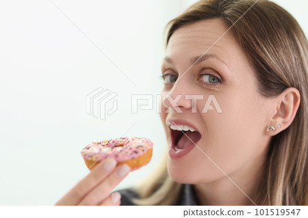 Woman bites delicious donut with glaze looking in camera 101519547