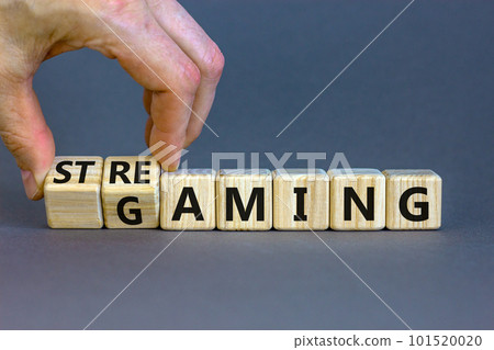 Gaming and streaming symbol. Businessman turns wooden cubes and changes the word gaming to streaming. Beautiful grey table grey background, copy space. Business, gaming and streaming concept. 101520020