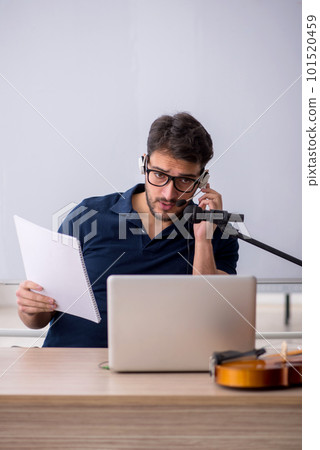 Young male music teacher sitting in the classroom 101520459