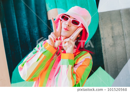 Urban Fresh street fashion look. Vanilla Girl. Kawaii vibes. Candy colors design. Bucket hat trends. Young woman with pink hair and sun glasses in multicolor strippled shirt on the wall background 101520568