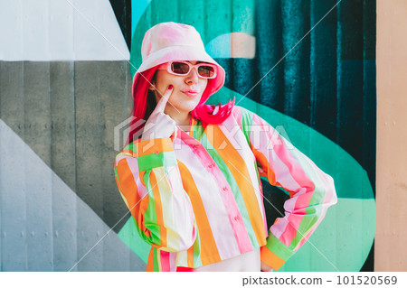 Urban Fresh street fashion look. Vanilla Girl. Kawaii vibes. Candy colors design. Bucket hat trends. Young woman with pink hair and sun glasses in multicolor strippled shirt on the wall background 101520569