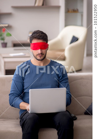 Blindfolded young male freelancer working from home 101522950
