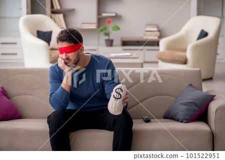 Young blindfolded man holding moneybag at home 101522951